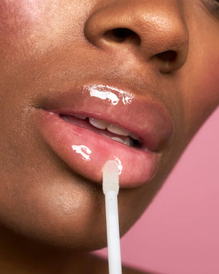 Artistic shot of a model holding the EM Cosmetics Crystal Lip Gloss, highlighting the product's minimalist packaging.