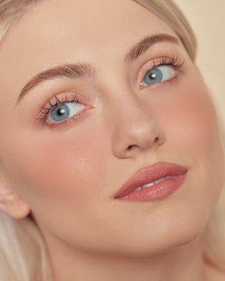 Model with light skin wearing EM Cosmetics Pillow Plush Blush in Peanut for a warm flush.