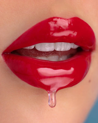 Model with light-medium skin shows the wet-look finish of EM Cosmetics Morning Dew Crystal Lip Gloss in Quartz.