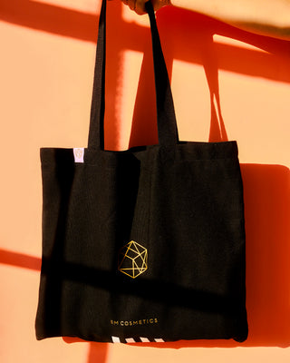 A stylish, minimalist white canvas tote bag with the black EM Cosmetics logo, perfect for carrying daily beauty essentials.